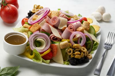 An antipasto salad with croutons and dressing on the side