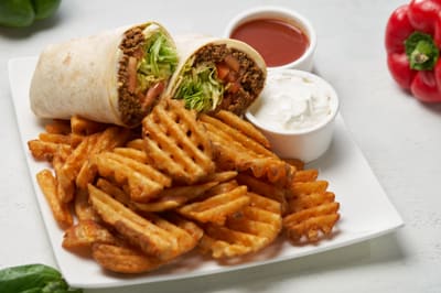 A beef taco wrap cut in half, served with waffle fries and sour cream