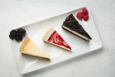 Plain, strawberry and Oreo cheesecake slices plated with fresh berries