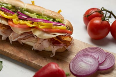 A cold sub with sliced meats, cheese, tomato, banana peppers and onion