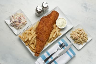 A fish fry plated with tartar sauce, cole slaw and macaroni salad