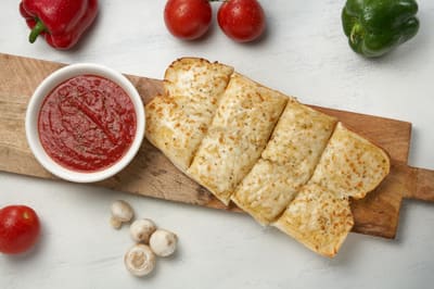 Garlic bread on a board with a bowl of dipping sauce