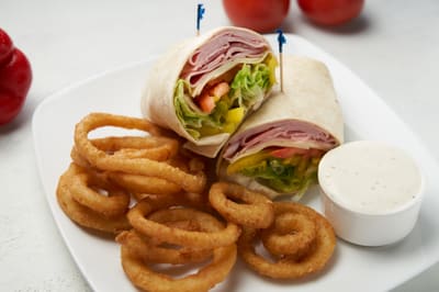 A ham wrap cut in half, served with onion rings and dipping sauce
