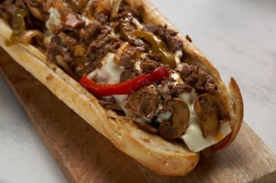 A steak hoagie with mushrooms, peppers and melted cheese