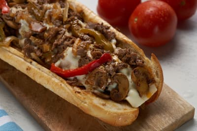 A steak hoagie on a wooden board with mushrooms and peppers