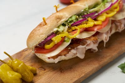 A turkey bacon sub on a wooden board with pepperoncini